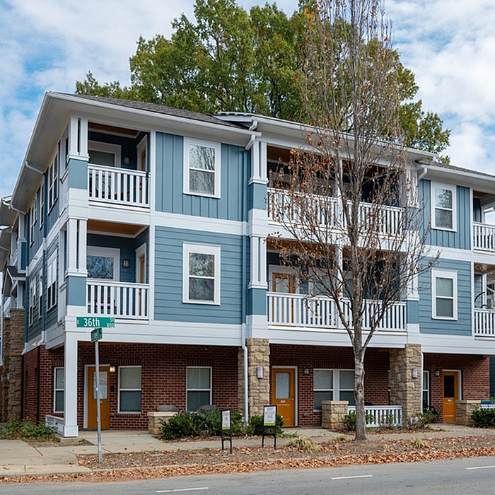 Charming modern apartment complex with blue siding, spacious balconies, and cozy brick accents in a serene neighborhood setting.