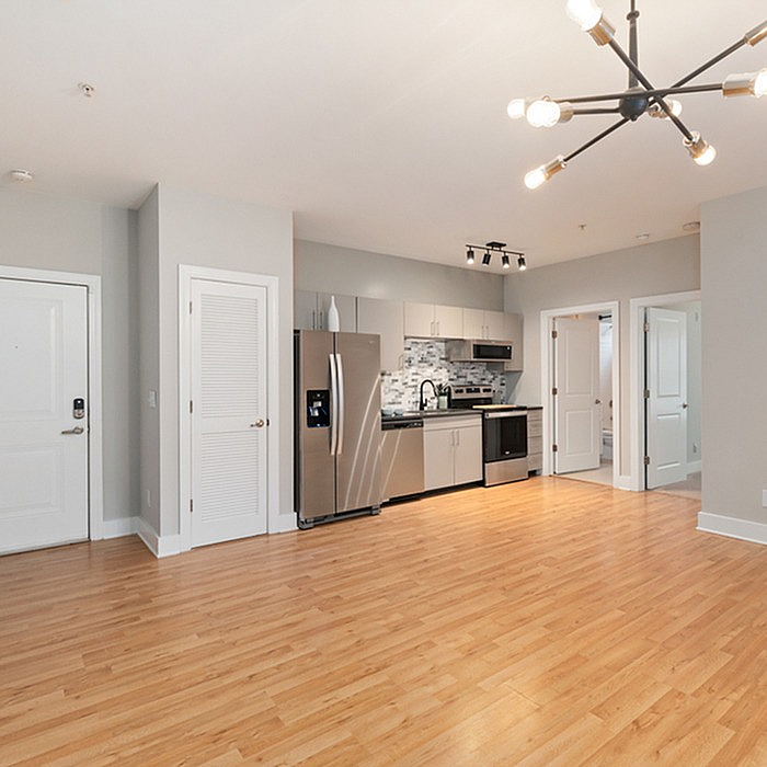 Modern open-plan kitchen and living area with sleek stainless steel appliances, wooden flooring, and stylish lighting fixtures.