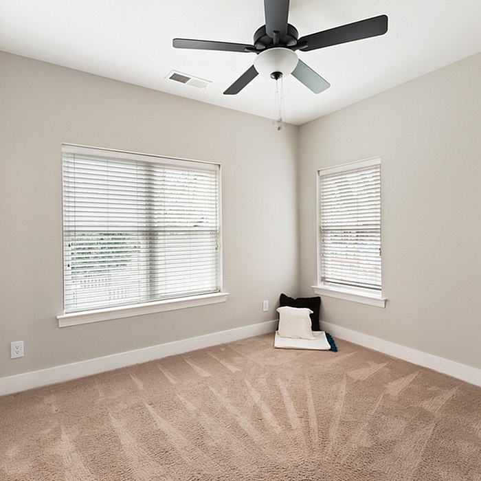 Bright, airy room with plush carpeting, large windows, and ceiling fan, perfect for comfortable living.