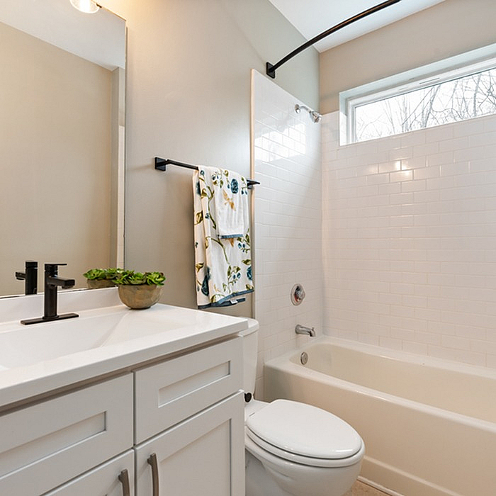 Elegant bathroom with white cabinetry, stylish fixtures, and a well-lit bathtub area featuring a modern shower.