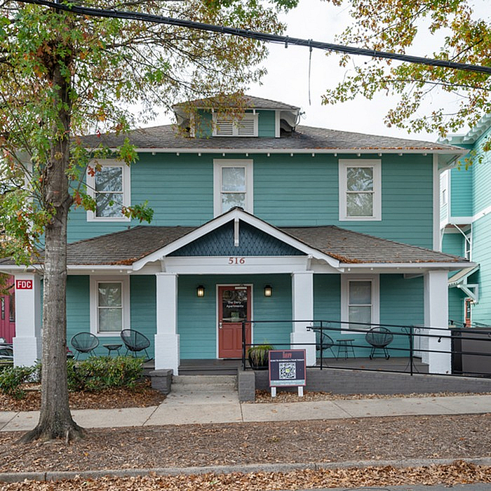 Charming teal-painted house with a welcoming front porch and stylish seating, surrounded by mature trees and vibrant greenery.
