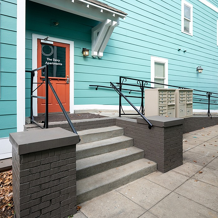 Charming apartment building entrance with vibrant teal siding and a welcoming red door at The Davy Apartments.