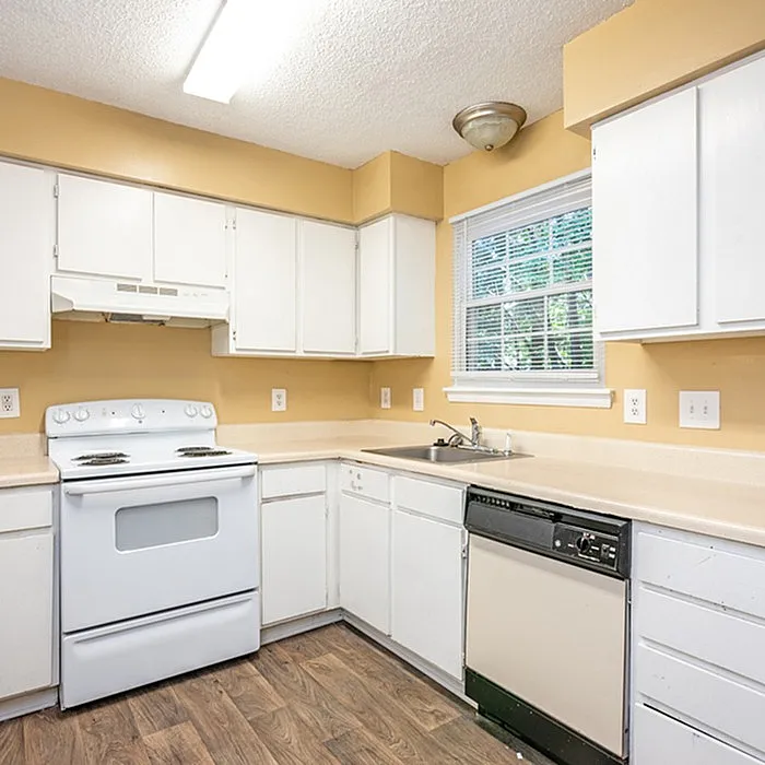 Bright kitchen with modern white cabinetry, efficient appliances, and warm wood flooring, ideal for culinary creativity.