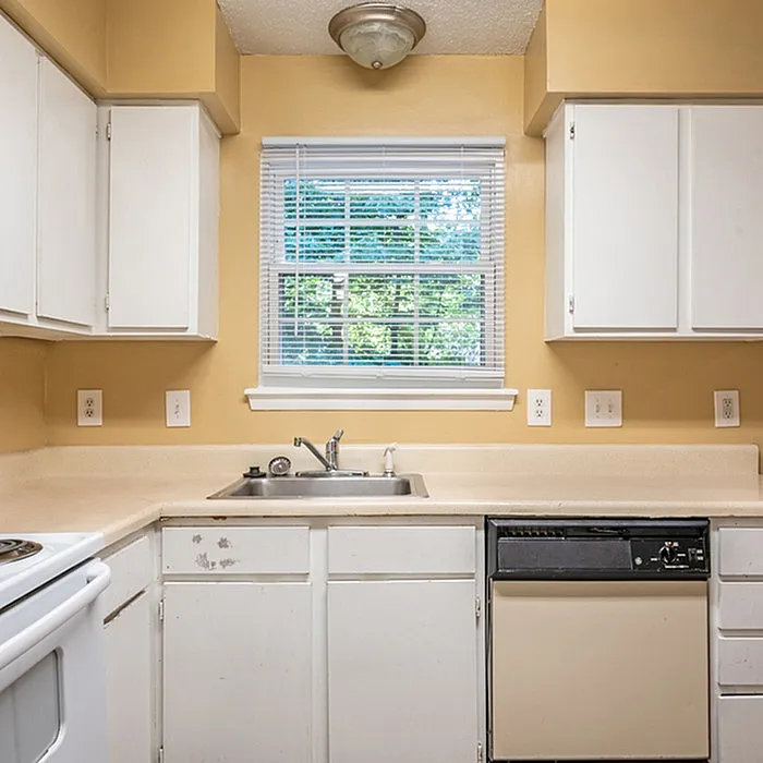 Cozy kitchen with warm beige walls, white cabinetry, and a double sink beneath a bright window.