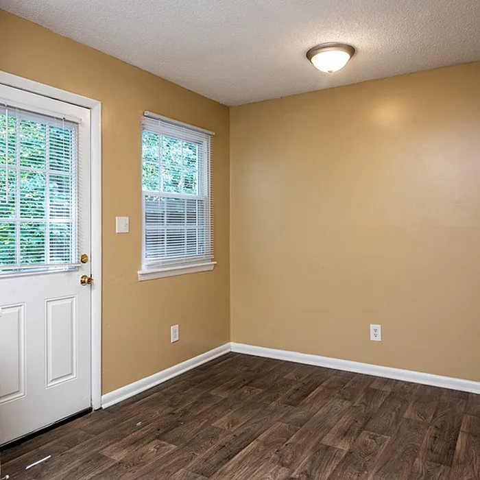 Inviting room with warm-toned walls, elegant wood flooring, and abundant natural light from a large window overlooking greenery.