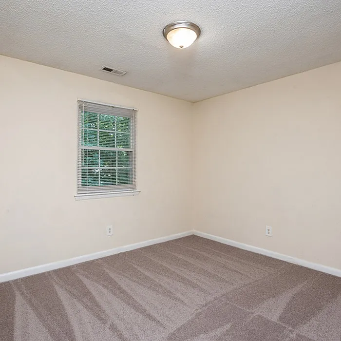 Bright, freshly carpeted room with a large window allowing abundant natural light, perfect for a cozy bedroom or home office.