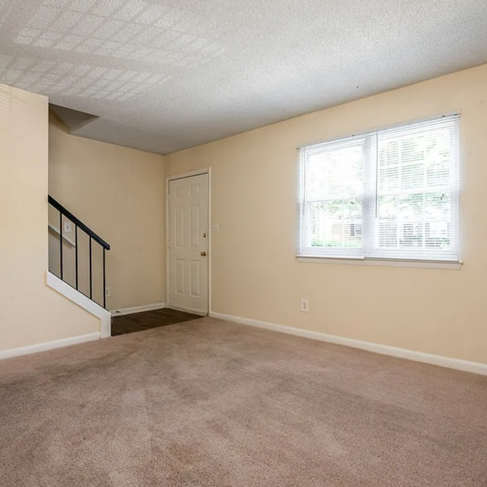 Bright, inviting living room with plush carpeting, large window for natural light, and elegant staircase.
