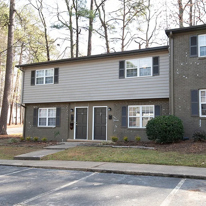 Charming two-story townhouse nestled among tall trees, featuring classic architecture and welcoming entryway.