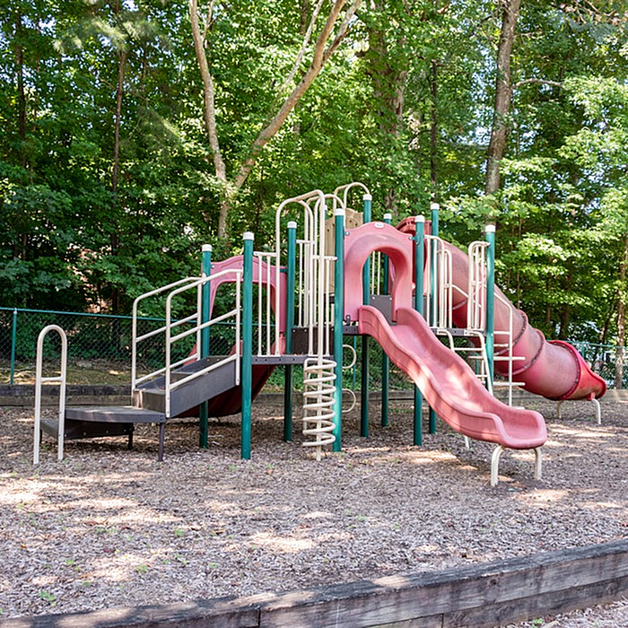 Charming playground featuring vibrant slides and tunnels surrounded by lush greenery. Ideal for family-friendly apartment living.