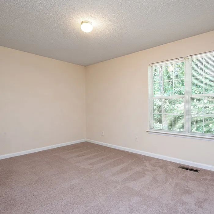 Bright and airy empty bedroom with plush carpet and large window offering serene outdoor views.