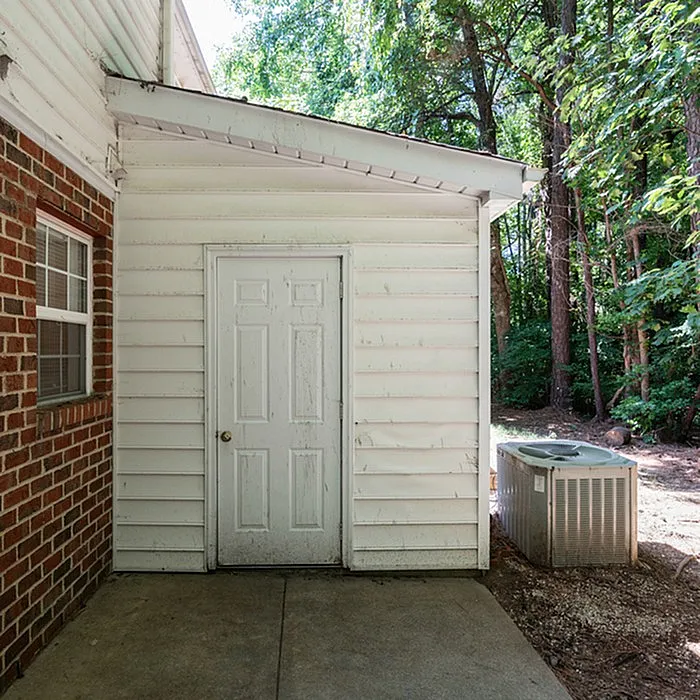 Charming house entrance with white siding and a serene wooded backdrop, offering a tranquil retreat.
