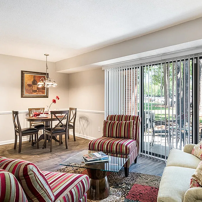 Chic living and dining area with stylish striped chairs, a glass-topped coffee table, and a dining set by the window offering bright, scenic views.