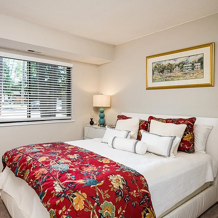 Inviting bedroom with a plush bed adorned with vibrant floral bedding, elegant decor, and natural light streaming through large windows.
