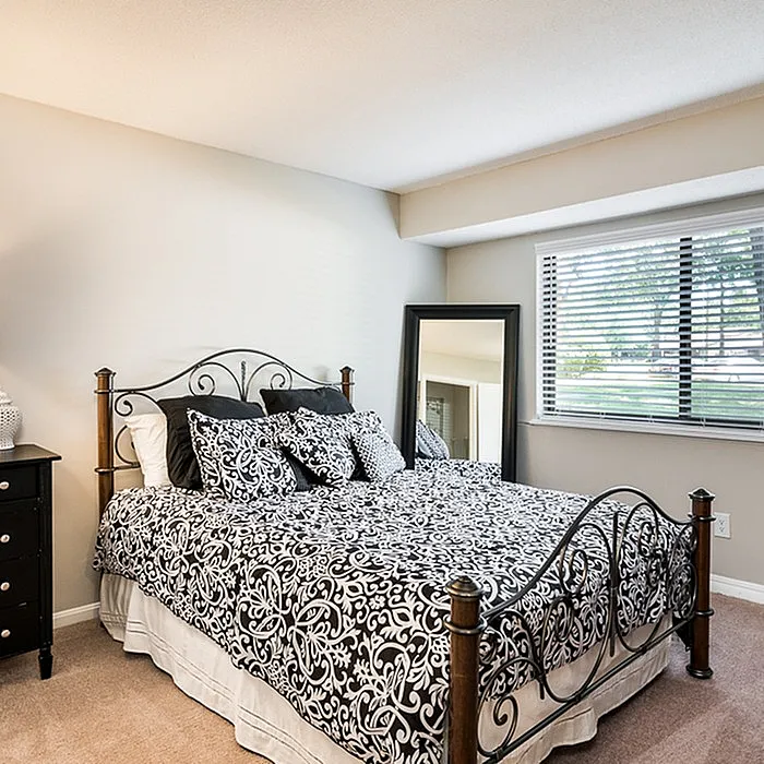 Inviting bedroom with elegant iron bed, stylish bedding, and large window offering natural light and garden views.