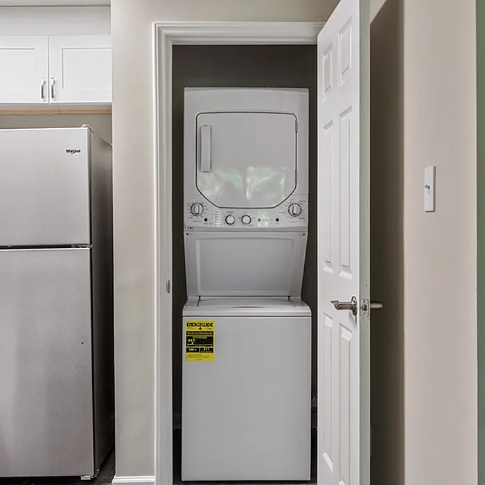 Convenient in-unit laundry with modern stacked washer and dryer beside a sleek stainless steel refrigerator.