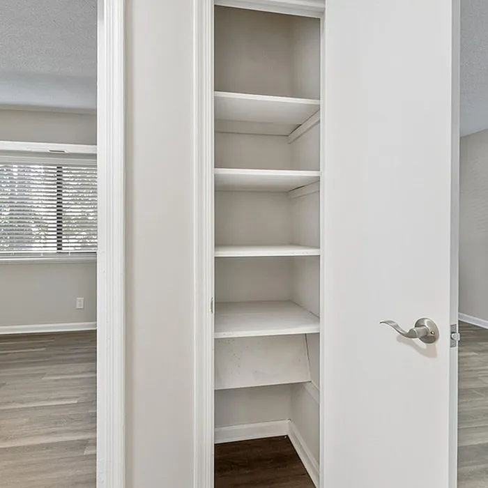 Modern apartment showcasing a spacious and sleek white closet with ample shelving, complemented by elegant hardwood floors and bright natural lighting.