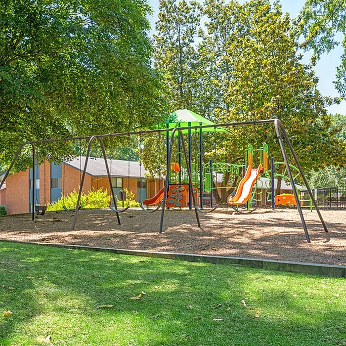 Vibrant playground with swings and slides nestled in a lush, green community setting, ideal for family-friendly living.