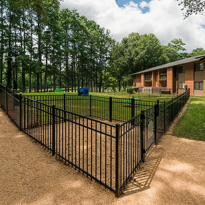 Inviting outdoor pet area with secure fencing, set in a lush green space next to charming brick apartments.
