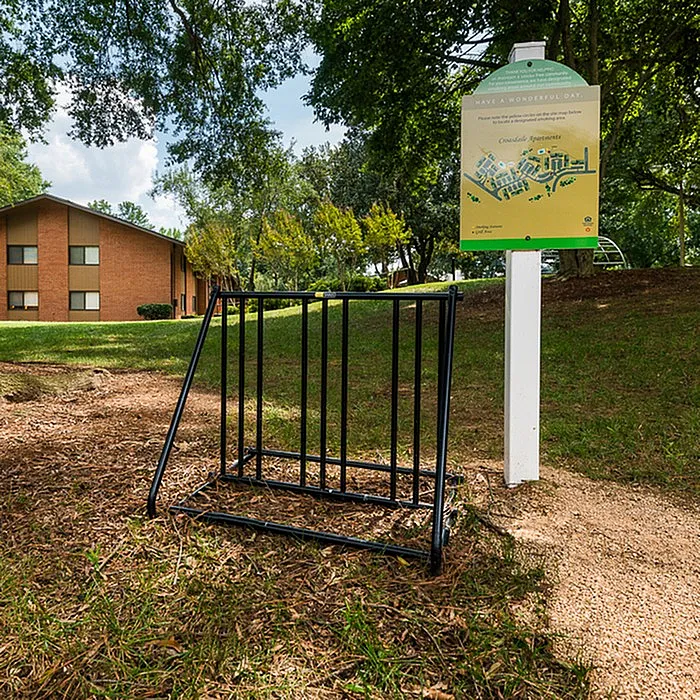 Charming apartment exterior with lush greenery, bike rack, and informational sign in a serene setting.