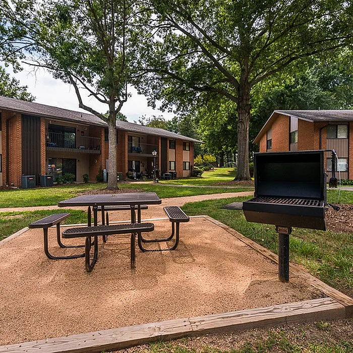 Charming apartment complex featuring lush greenery, picnic area with benches, and outdoor barbecue space.