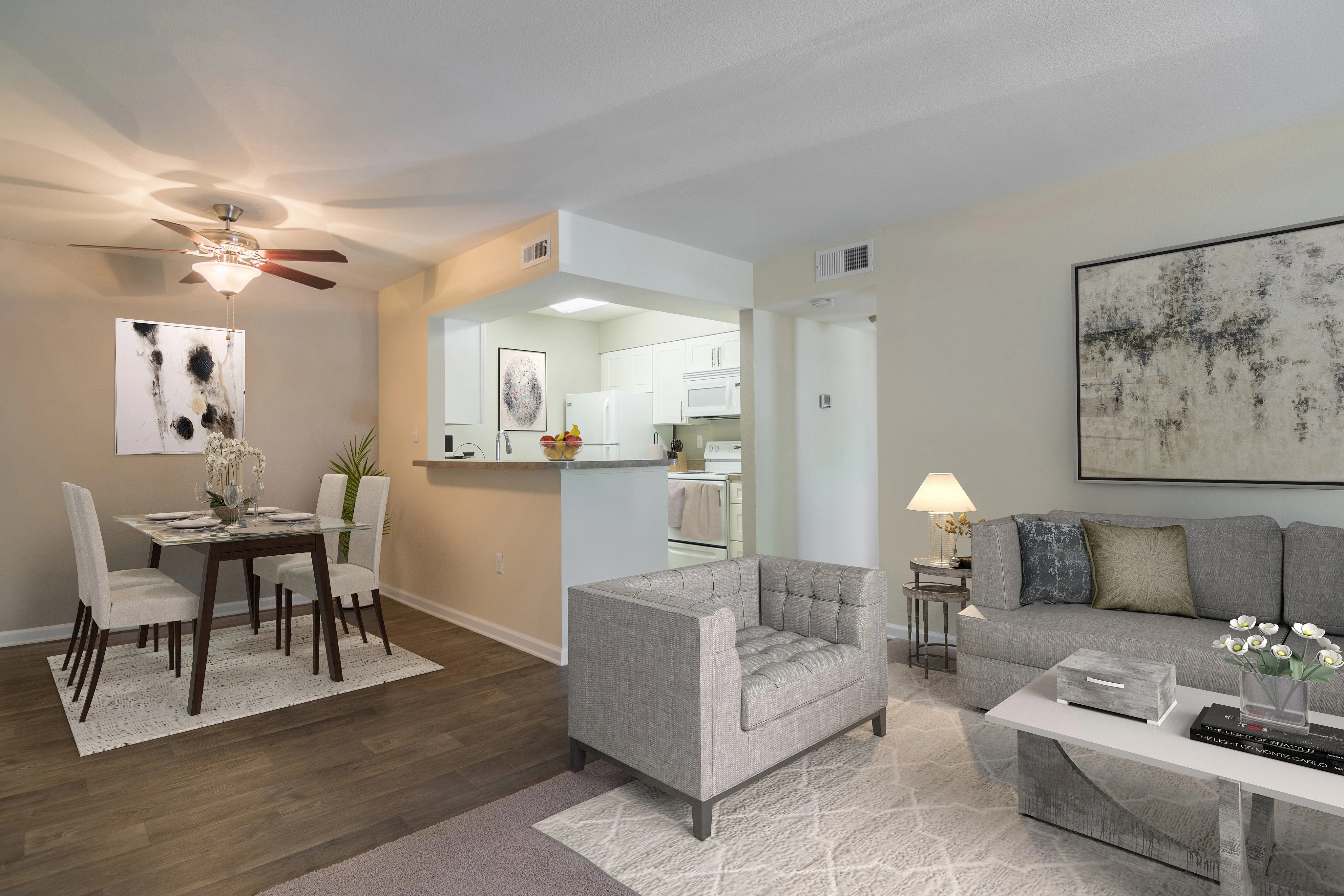 Modern open-concept living and dining area with elegant furnishings, cozy gray sofa, sleek armchair, and stylish decor. Bright kitchen with white cabinetry completes the inviting space.