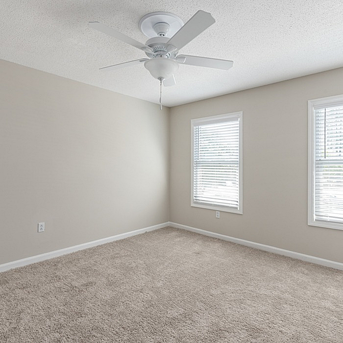 Bright and airy bedroom featuring soft carpet, two windows with blinds, and a modern ceiling fan.