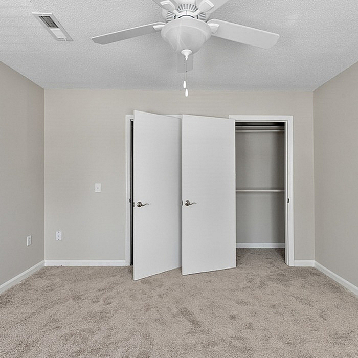 Bright and airy bedroom with plush carpeting, featuring a ceiling fan and spacious closet with double doors.