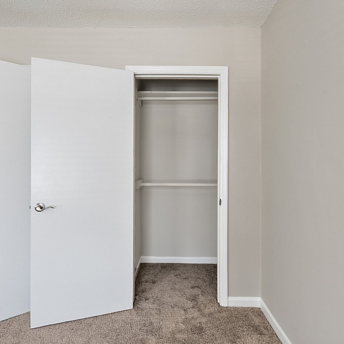 Spacious walk-in closet with neutral gray walls and plush carpet flooring, ideal for organized storage.