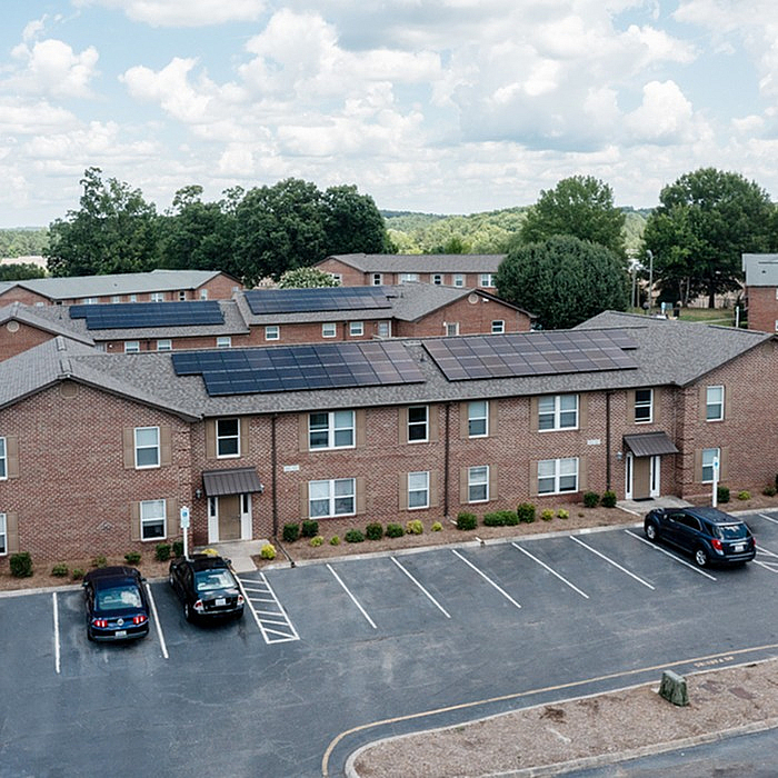 Modern apartment complex with solar panels, spacious parking, and lush greenery under a clear sky.