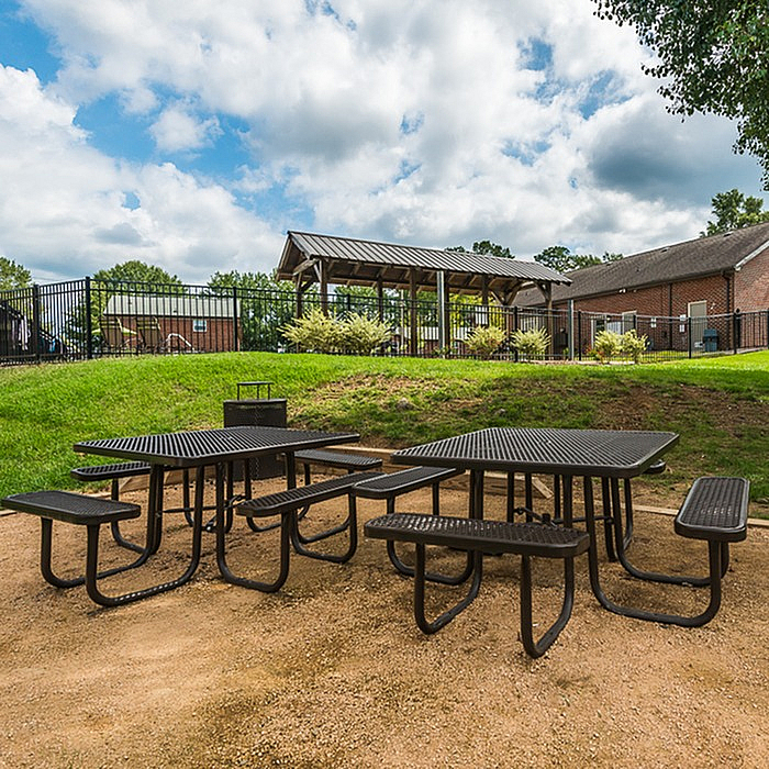 Charming outdoor picnic area with modern black benches set against a lush green backdrop and a stylish wooden pergola.