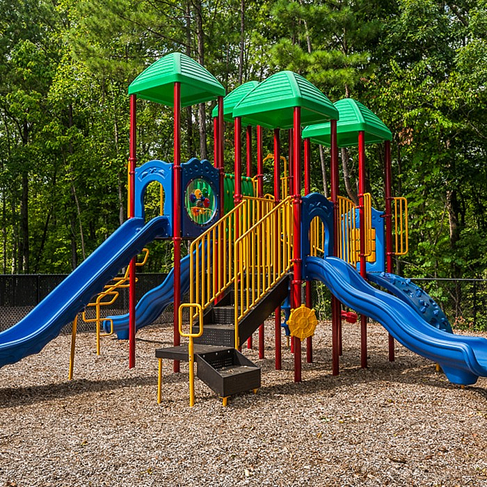 Vibrant playground with multi-colored slides and climbing structures surrounded by lush trees, offering a perfect family-friendly outdoor environment.