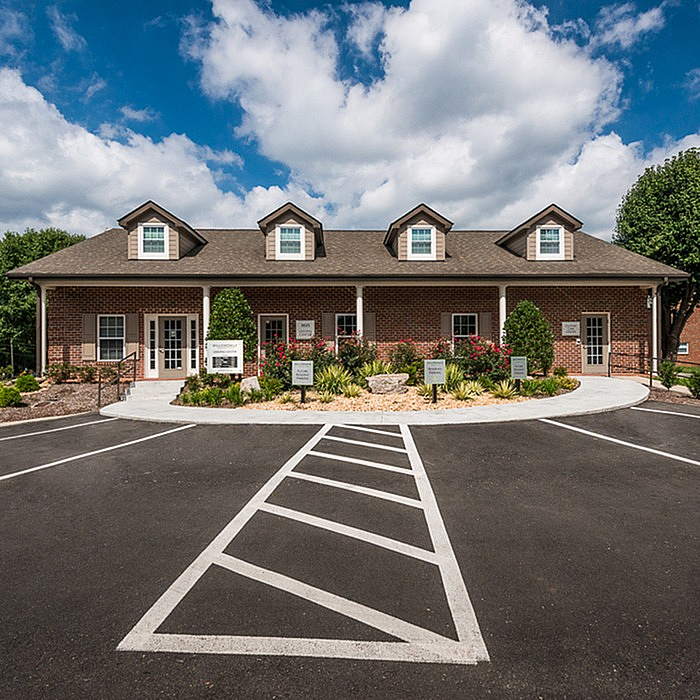 Charming brick building with dormer windows and welcoming landscaping under a bright blue sky.