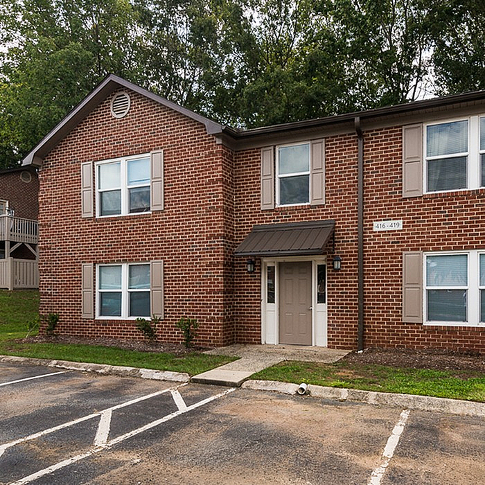 Charming brick apartment building with stylish shutters and lush greenery, offering a welcoming entrance and ample parking.