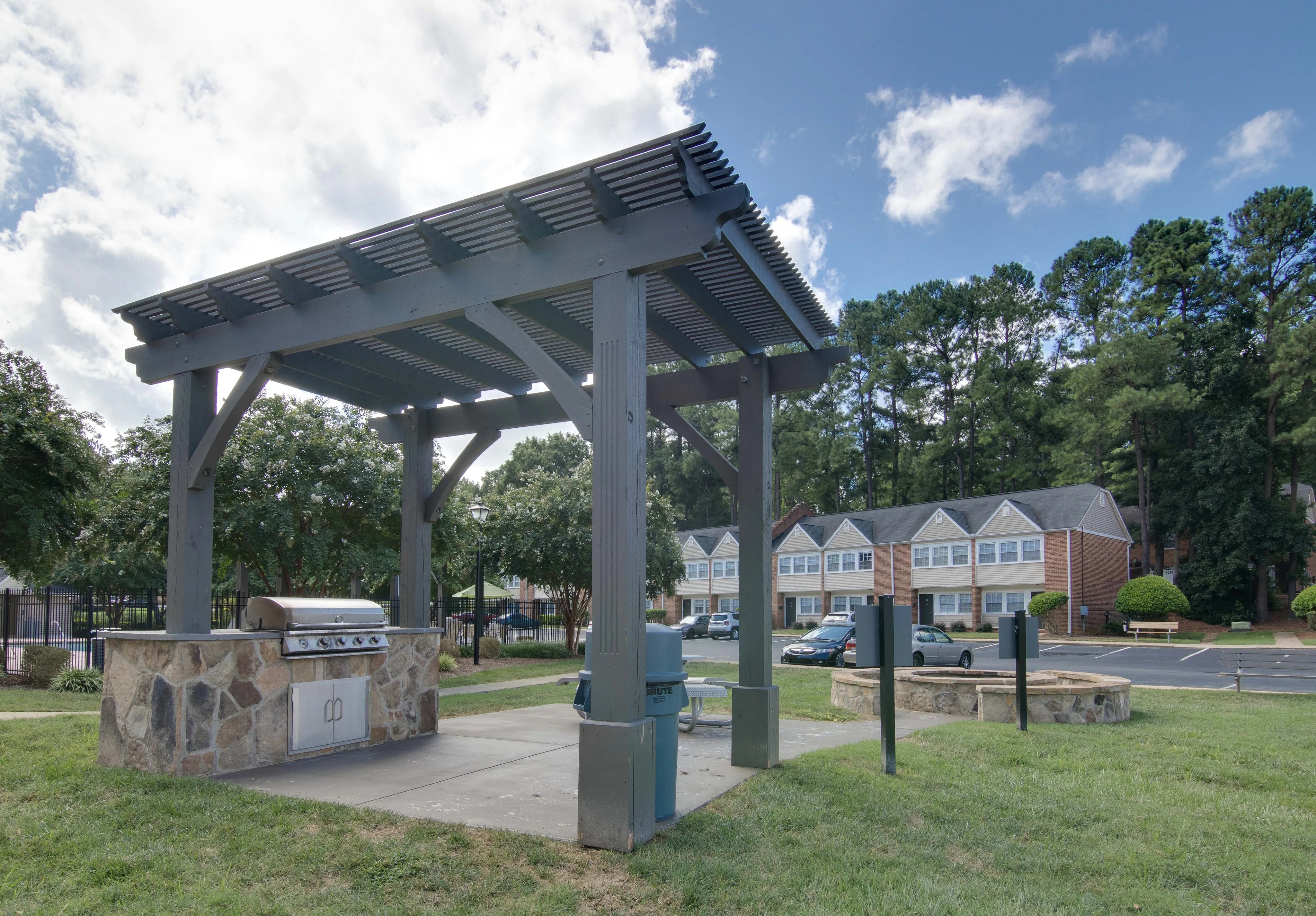Inviting outdoor grilling area with a pergola and stone BBQ setup, surrounded by lush greenery and charming townhouses.
