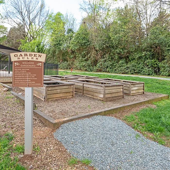 Charming community garden with well-maintained raised wooden planters, surrounded by lush greenery and a welcoming sign.