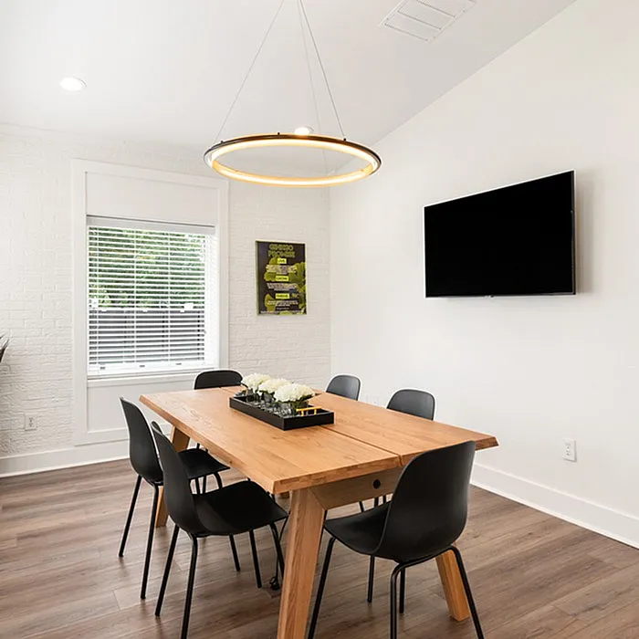 Elegant dining room featuring a modern wooden table, sleek black chairs, and a striking circular light fixture, enhanced by natural light from a large window.