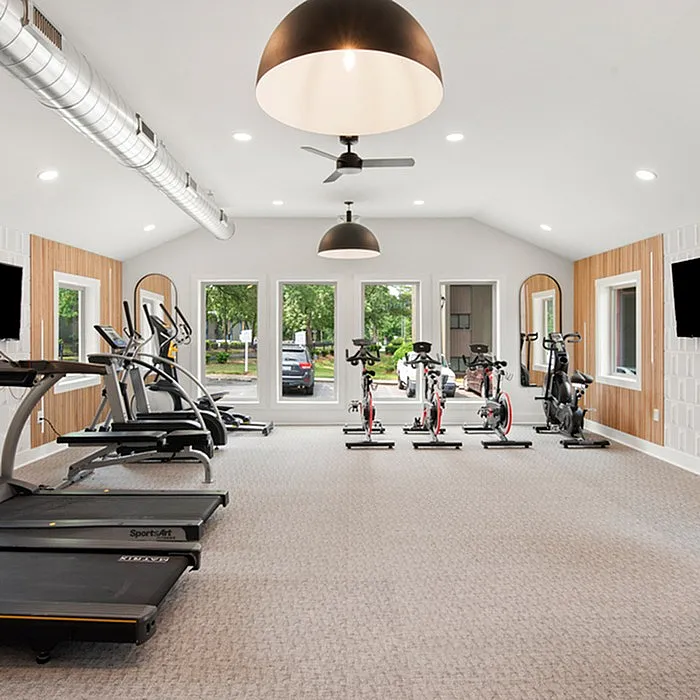 Modern fitness center with state-of-the-art treadmills, exercise bikes, and large windows offering lush garden views.