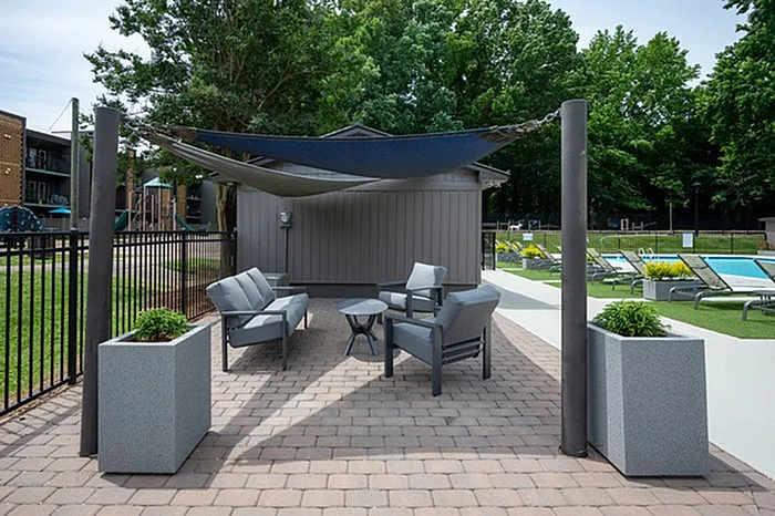 Modern outdoor seating area with sleek chairs, stylish canopy, and lush poolside loungers, creating a relaxing oasis.