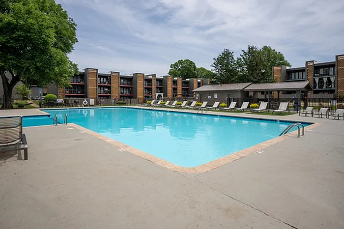 Inviting apartment complex with a large, refreshing swimming pool surrounded by sun loungers and lush greenery, perfect for relaxation and leisure.