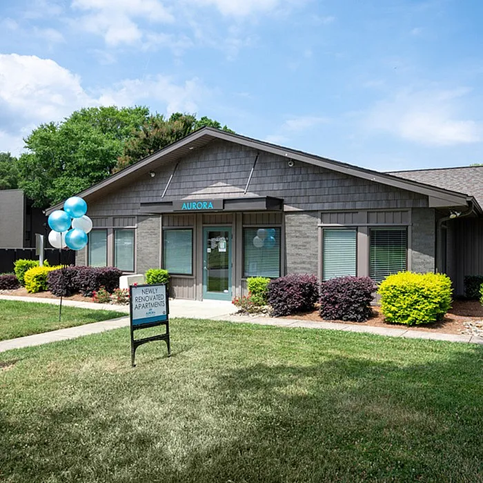 Charming apartment exterior with lush landscaping and inviting entrance, featuring vibrant balloons and a sign for newly renovated apartments at Aurora.