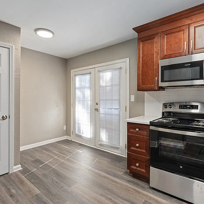 Bright kitchen with sleek stainless steel appliances, rich wooden cabinetry, and elegant French doors opening to a sunlit space.