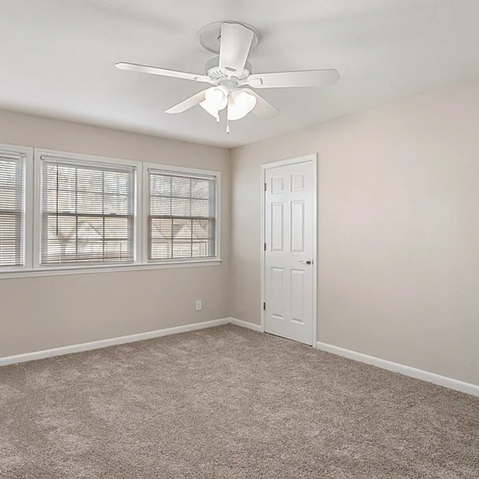 Bright, cozy bedroom with plush carpet, modern ceiling fan, and large windows offering natural light.