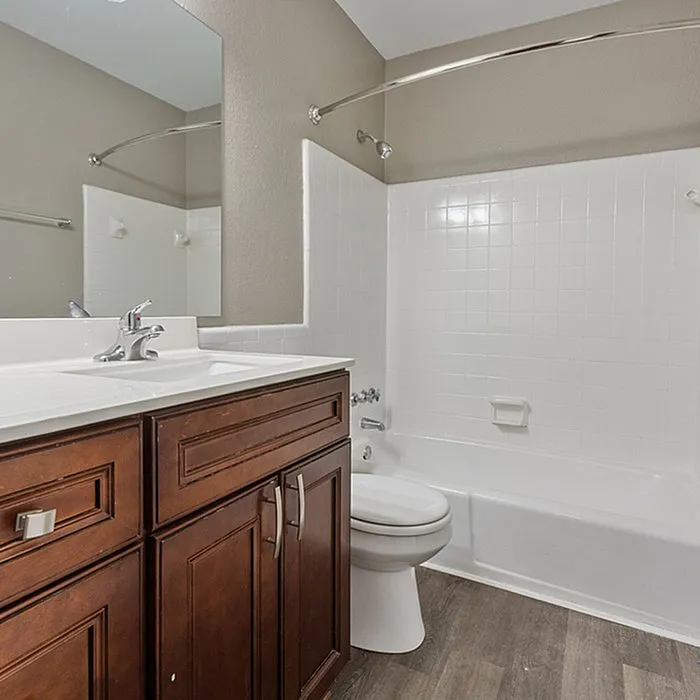 Elegant bathroom featuring modern fixtures, a sleek vanity with rich wood cabinetry, and a pristine white tiled bathtub, exuding contemporary charm.