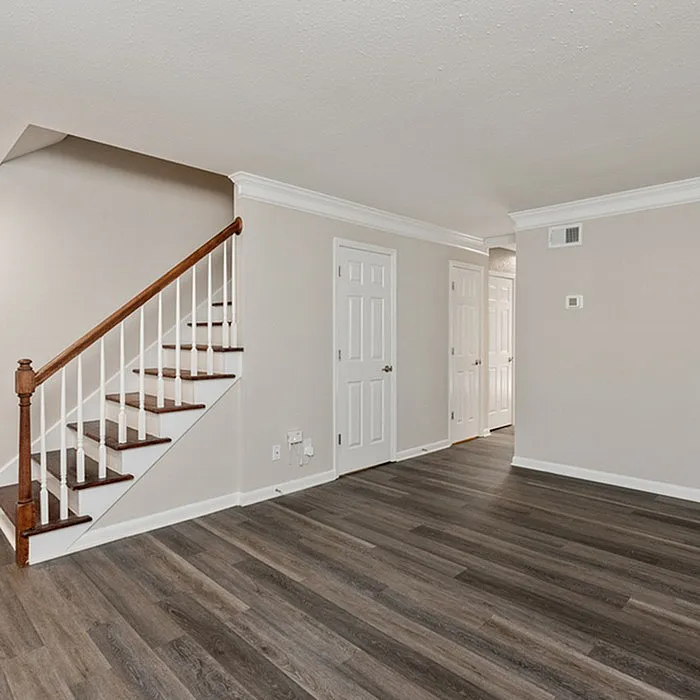 Elegant living space with modern hardwood floors, crisp white walls, and an inviting staircase with wooden railing.