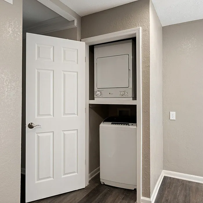 Compact laundry nook featuring a stacked washer and dryer in a modern apartment with sleek wood flooring.