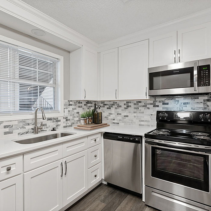 Contemporary kitchen boasting sleek stainless steel appliances, elegant white cabinetry, and a modern mosaic backsplash.