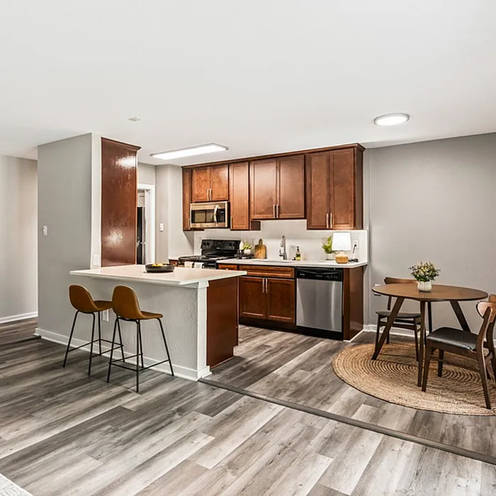 Modern, well-lit apartment kitchen with rich wood cabinetry, stainless steel appliances, and a cozy dining nook, creating a warm and inviting atmosphere.
