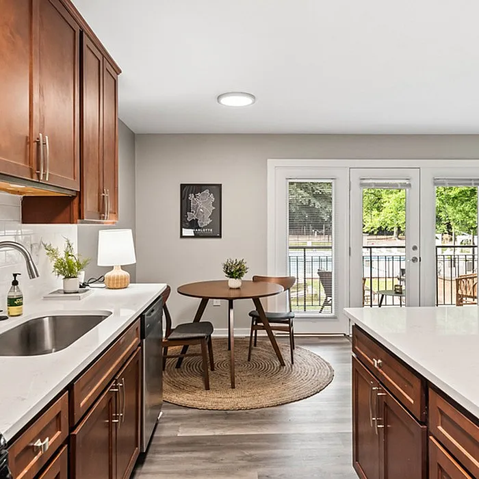 Inviting kitchen area with modern wooden cabinets, elegant countertops, and a cozy dining space overlooking a sunlit balcony.