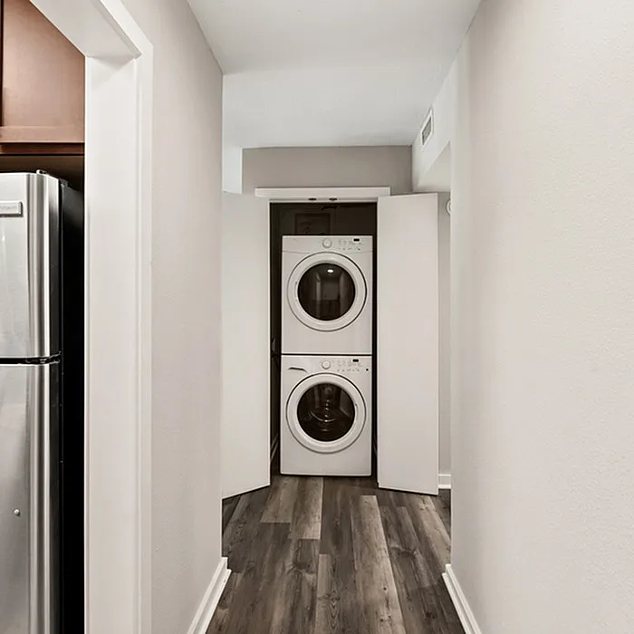 Modern apartment hallway featuring sleek laminate flooring and an in-unit stacked washer and dryer discreetly tucked behind folding doors.