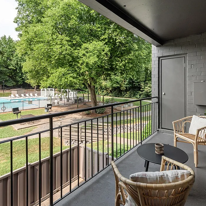 Charming apartment balcony with cozy seating overlooking a lush green oasis and refreshing swimming pool.